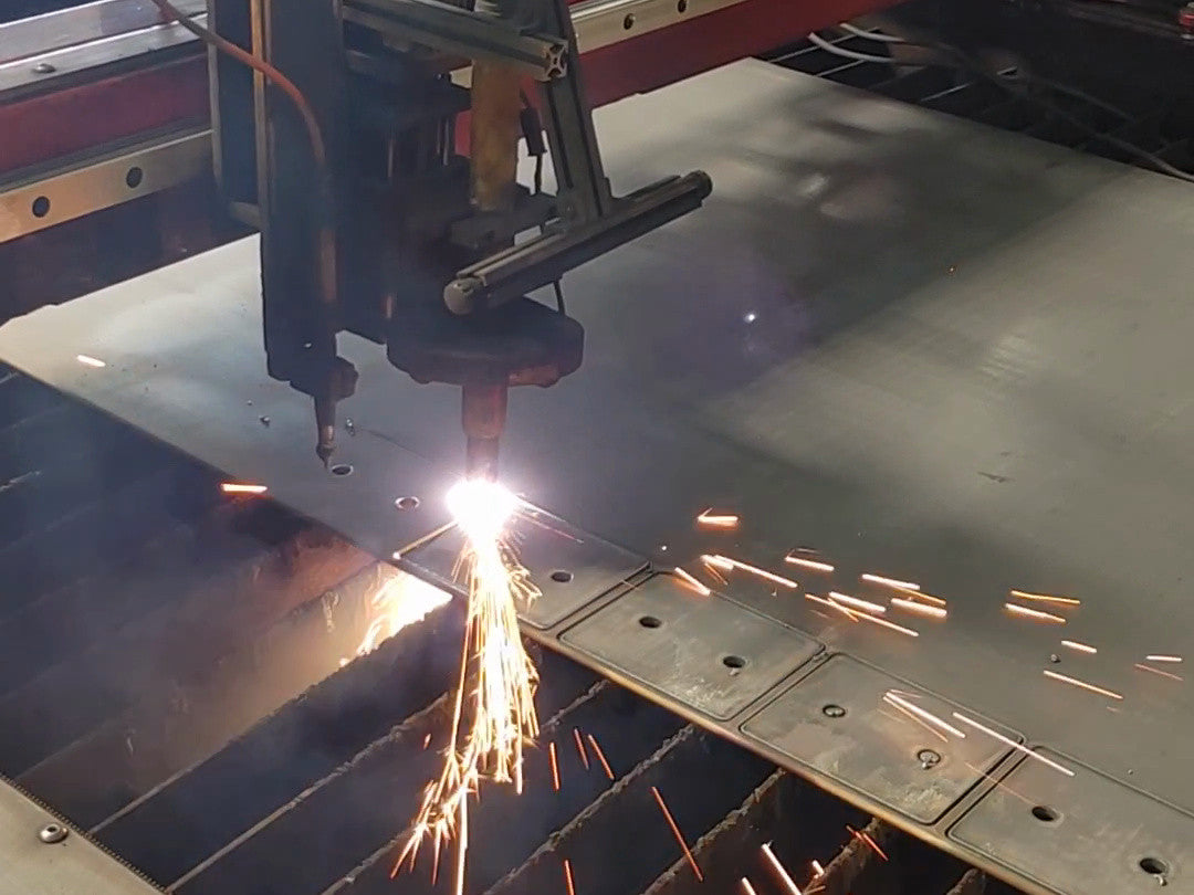 A CNC plasma table cutting EmberBox panels from sheet steel, sparks falling through the slats.