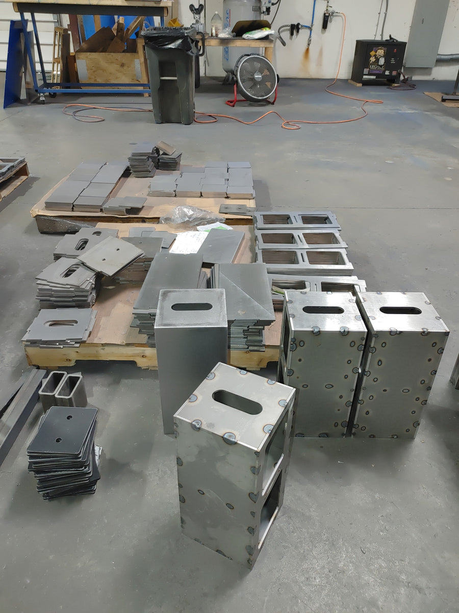 Tack-welded EmberBox shells beside pallets of flat panels.